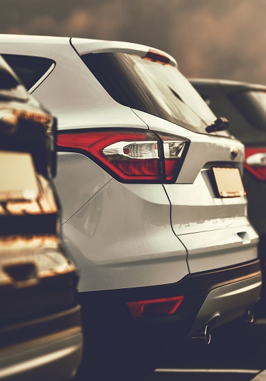 Arrière d'un SUV blanc moderne garé en rangée avec d'autres véhicules. Gros plan sur les feux arrière rouges et le pare-chocs.